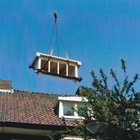 afbeelding: Prefab dakkappel, houten kozijn, kunststof bekleding, wordt met de kraan Backx Staal over het dak gedraaid.